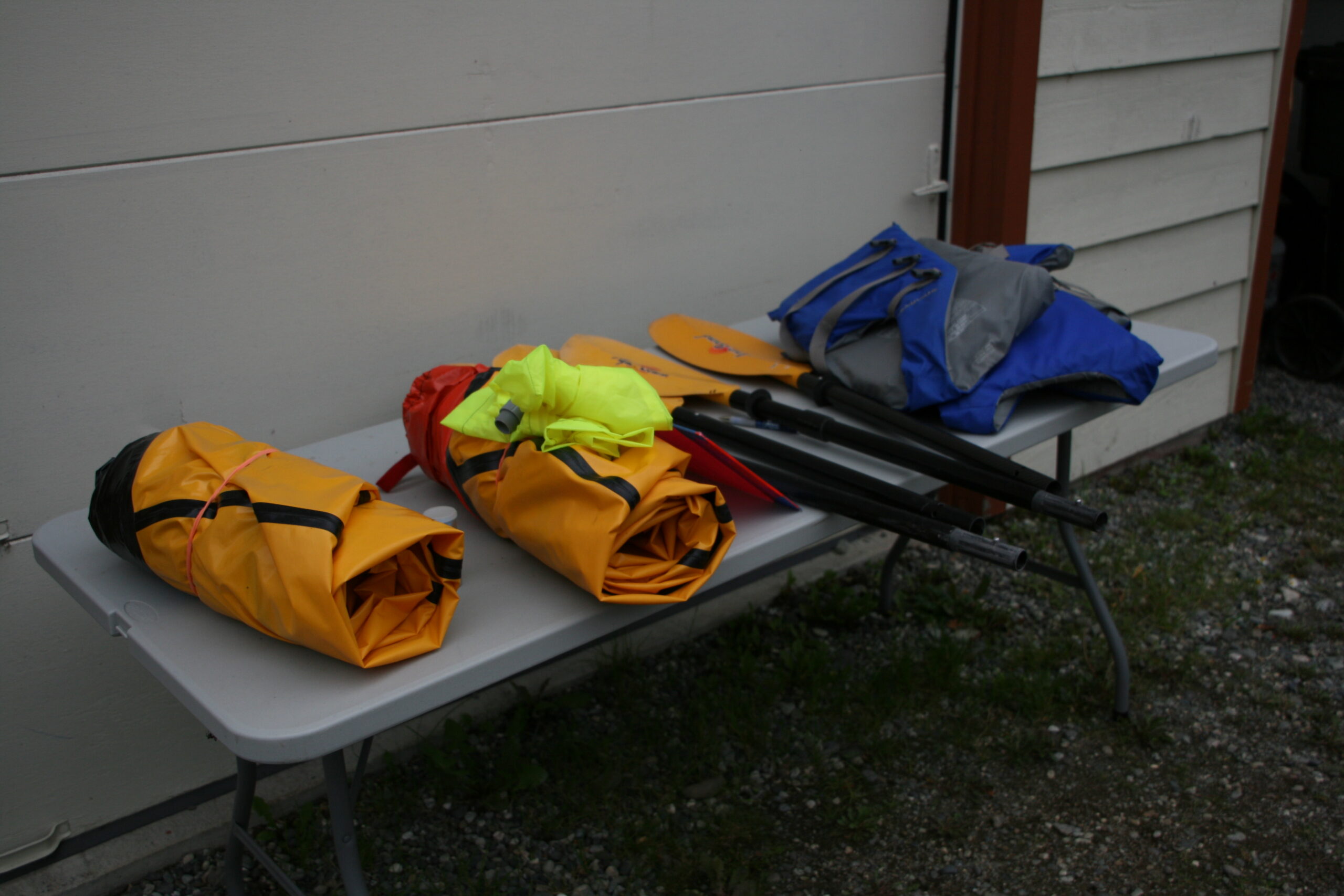 Packrafts, paddles, and life vests sit on a table ready to be packed.