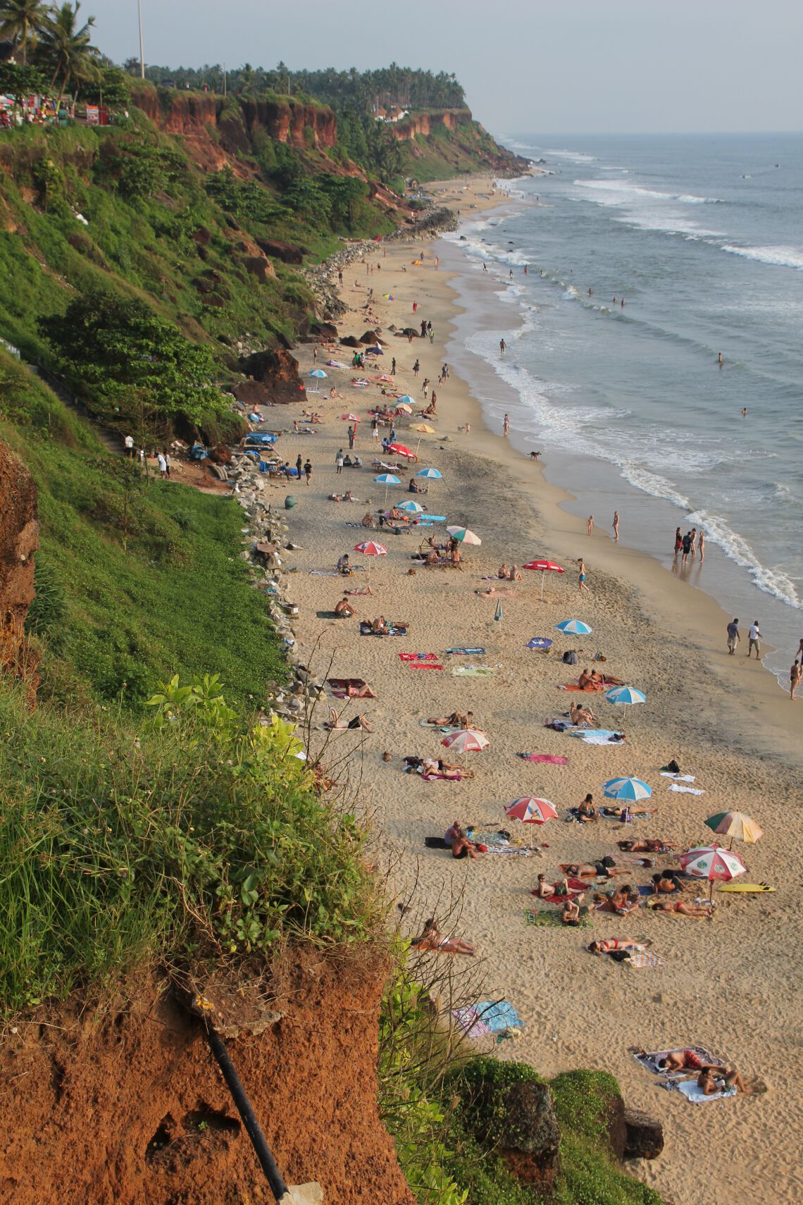 Tourists relax on the beach below cliffs in Varkala, India.