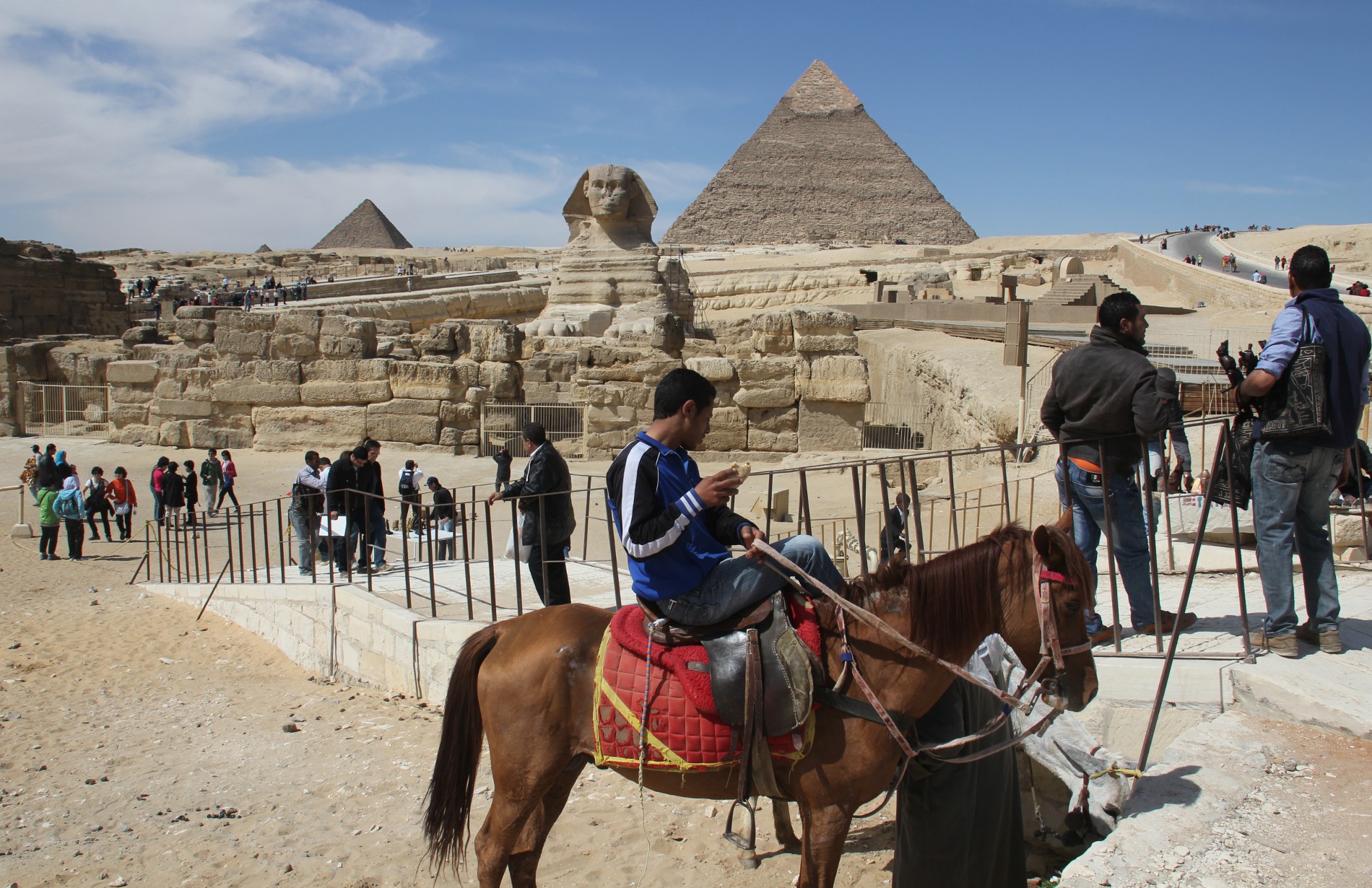 A man renting a horse waits for tourists in front of the Sphinx, the Chephren Pyramid, and the Mycerinus Pyramid.