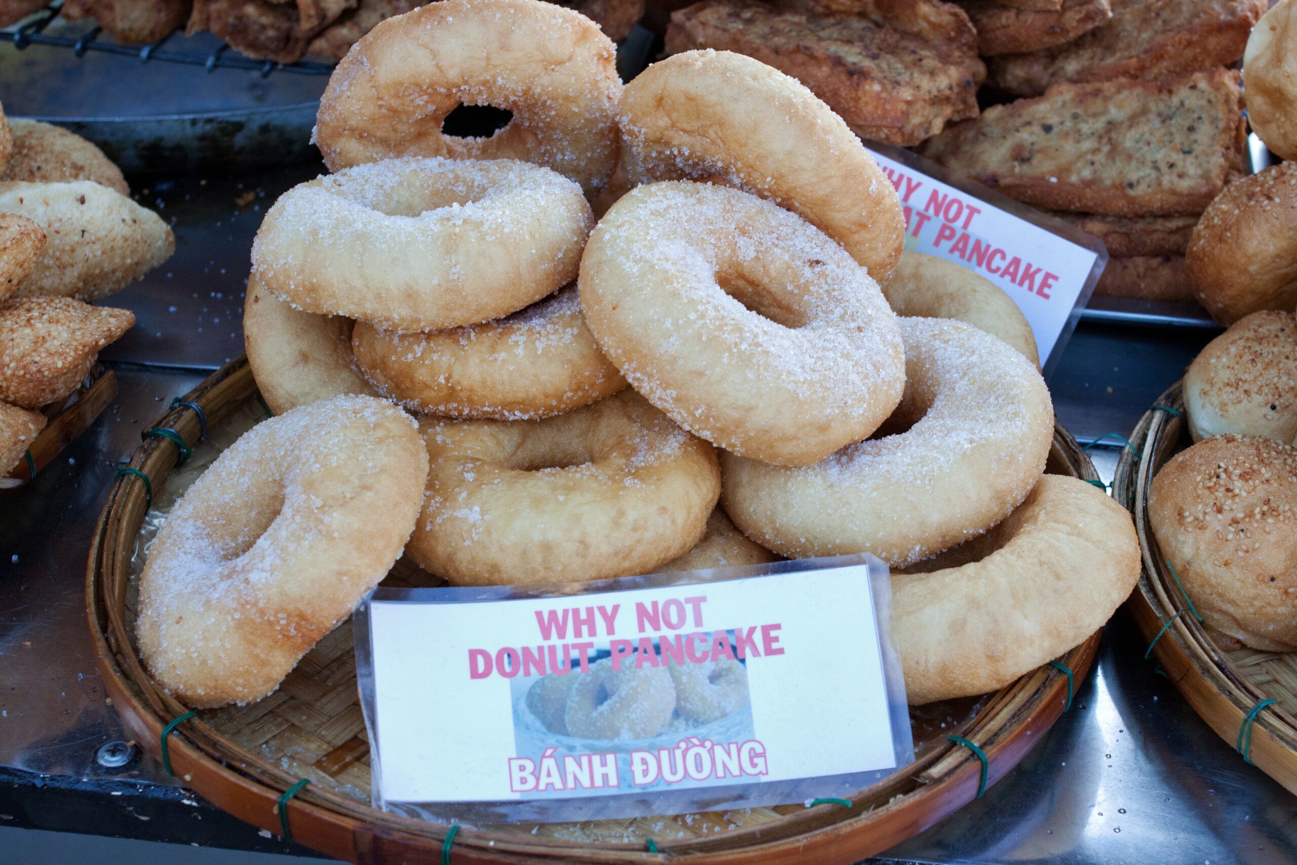 A "WHY NOT DONUT PANCAKE" sign sits in front of donuts for sale in Hoi An, Vietnam.