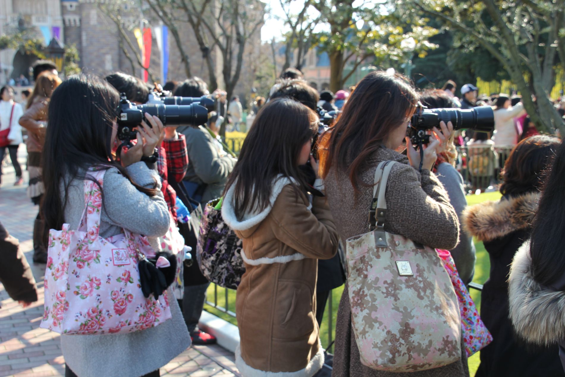 Women take photos of a parade at Tokyo Disneyland.