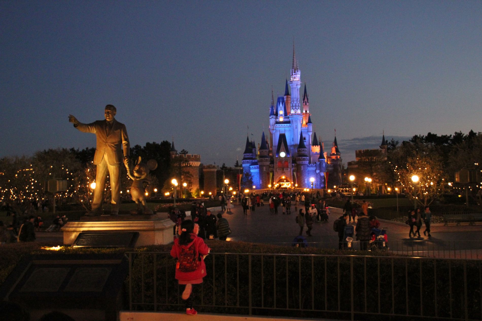 A young Japanese girl looks at Cinderella's Fairy Tale Hall in Tokyo Disneyland at night.