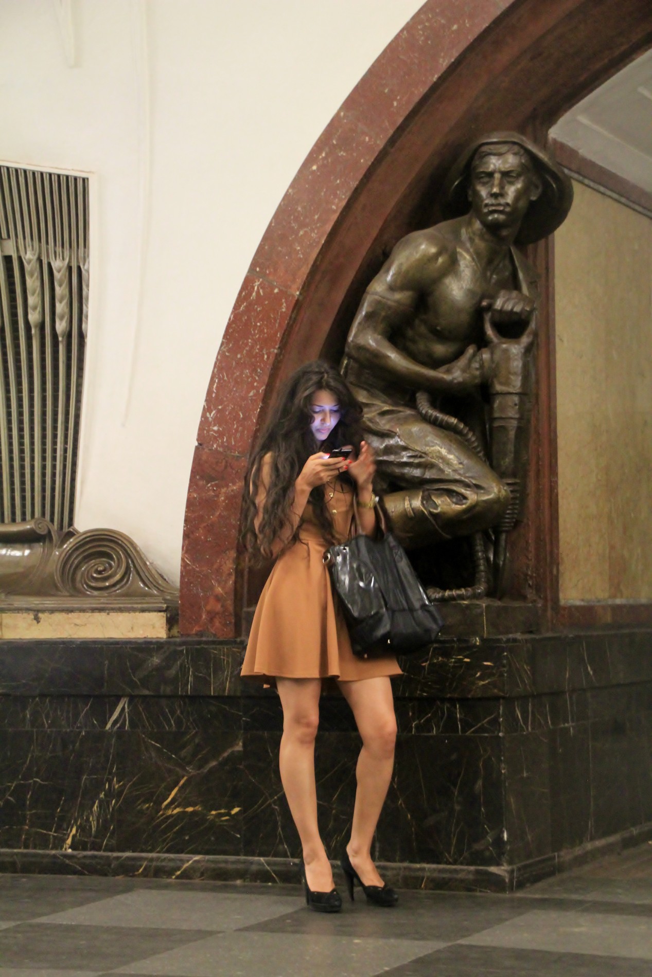 A Russian woman sends a text under a bronze statue of a miner at the Ploshchad Revolyutsii Moscow Metro station.