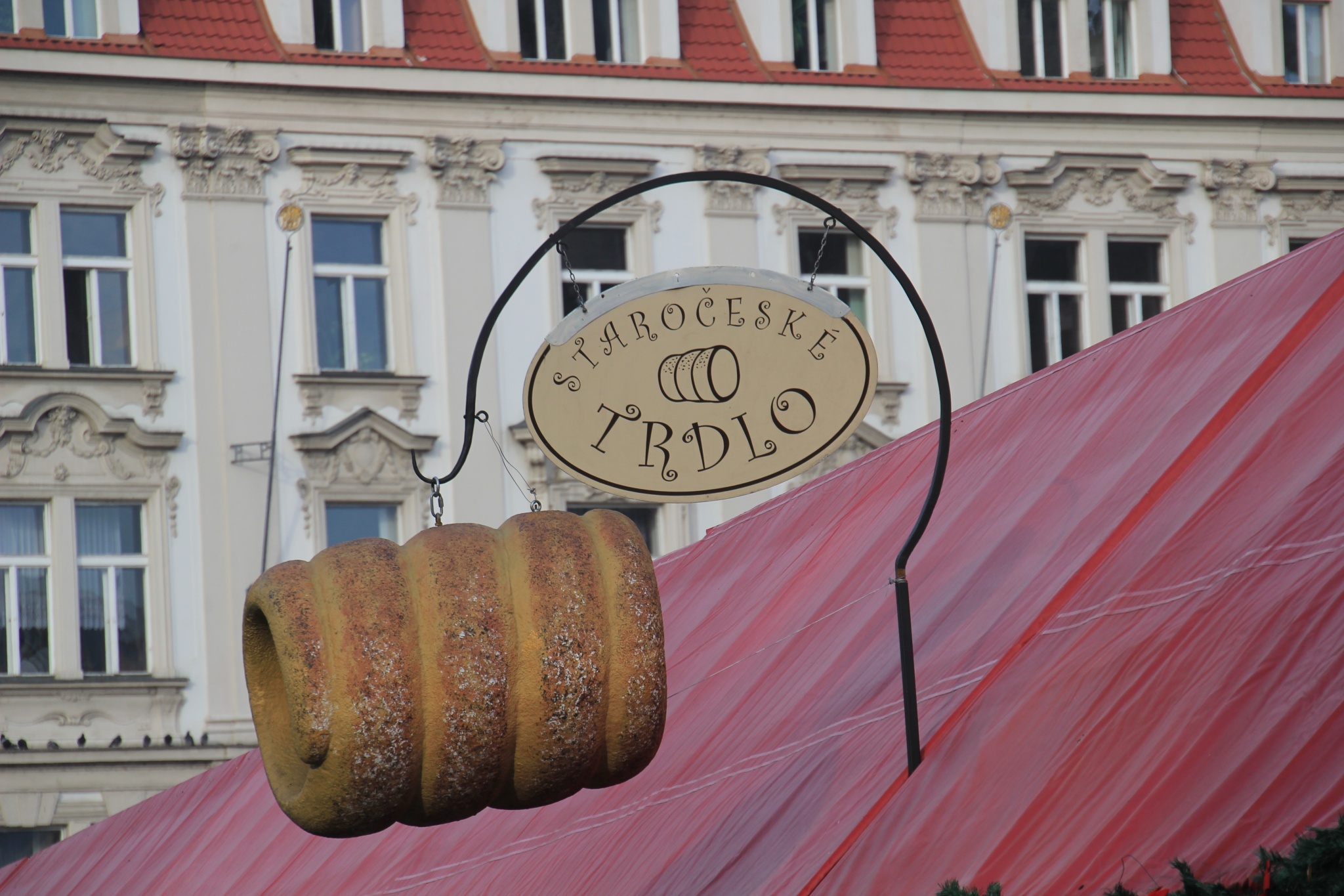 An enormous trdelnik hangs attached to a sign above a trdelnik vendor in Prague's Old Town Square.