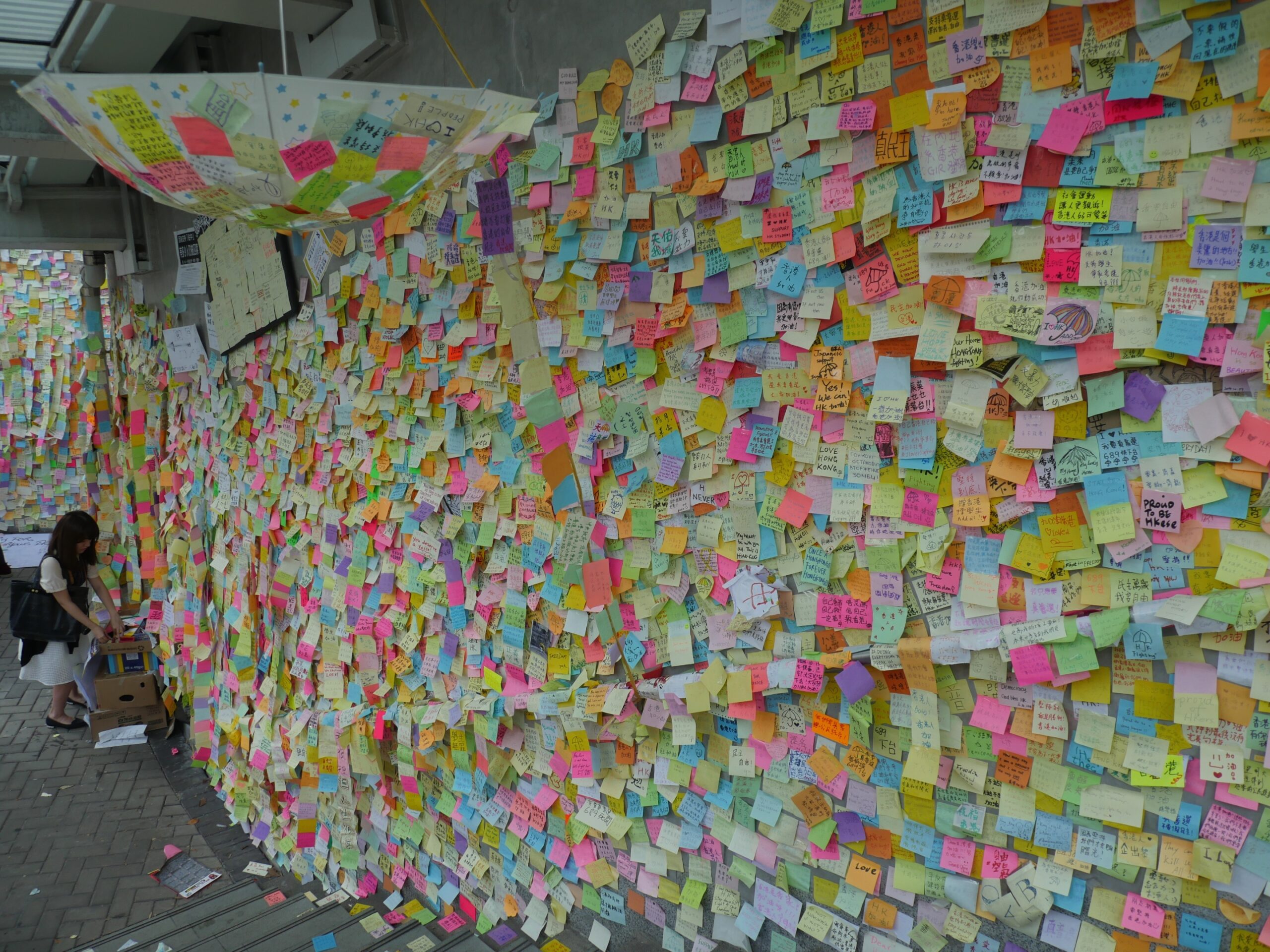 A woman adds a supportive message to the Lennon Wall Hong Kong.