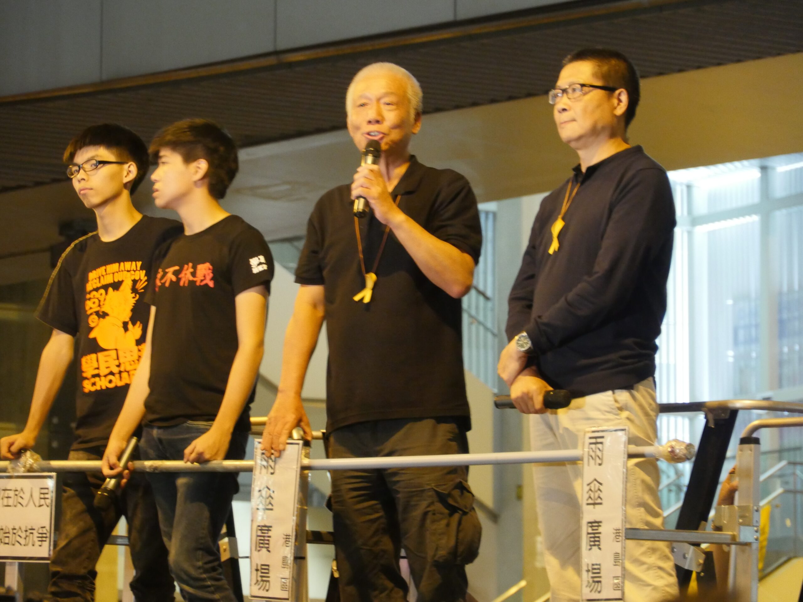 Occupy Hong Kong organizers Joshua Wong, Lester Shum, Chu Yiu-Ming, and Chan Kin-Man speak in front of a crowd.