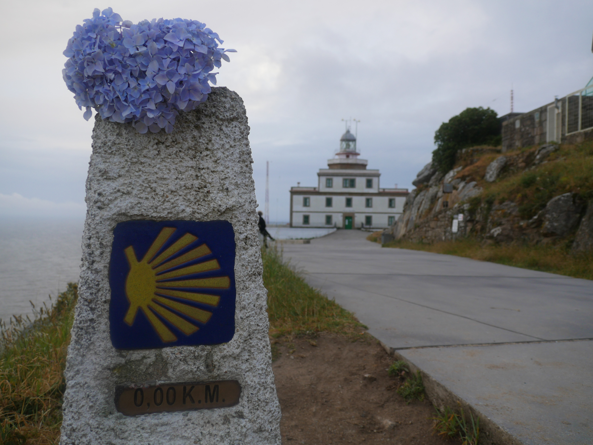 A stone marker labeled "0.00 K.M." marks the end of the Camino Finisterre at the end of the peninsula in Finisterre.