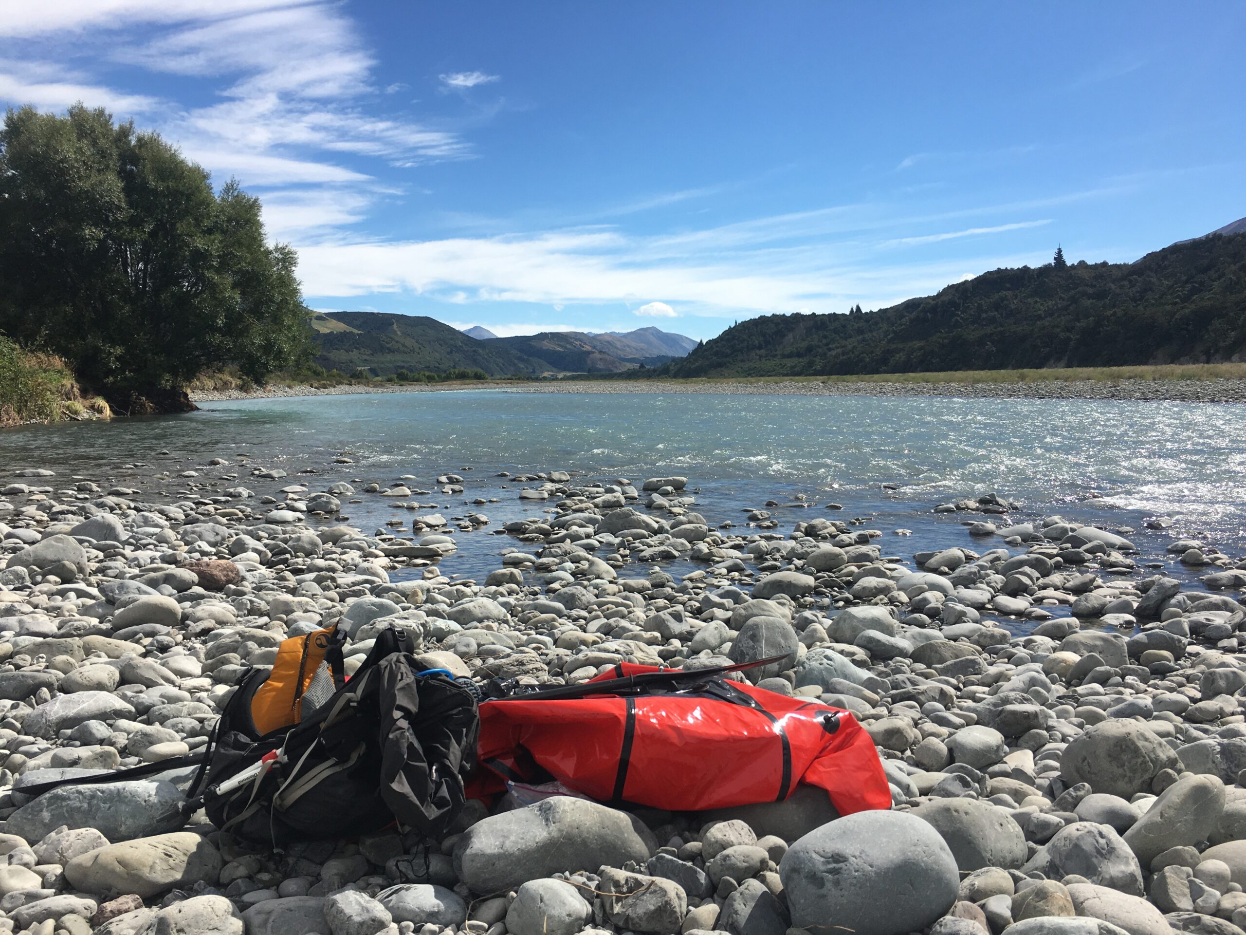 My packraft sits on the shore below the SH73 highway as I search for an access road to escape.